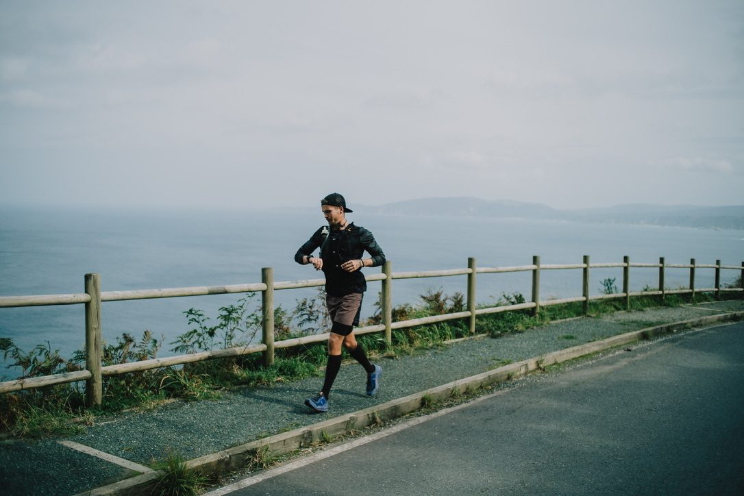 Jonathan Fors running a coastal road beside a wooden rail above the Atlantic.